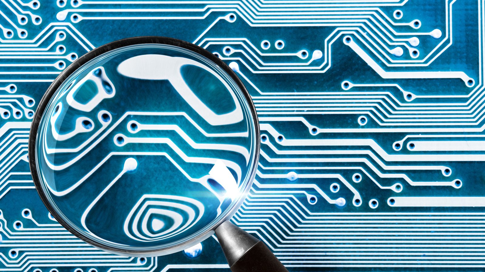 A magnifying glass held over a blue printed circuit board, enlarging the lines and dots underneath.