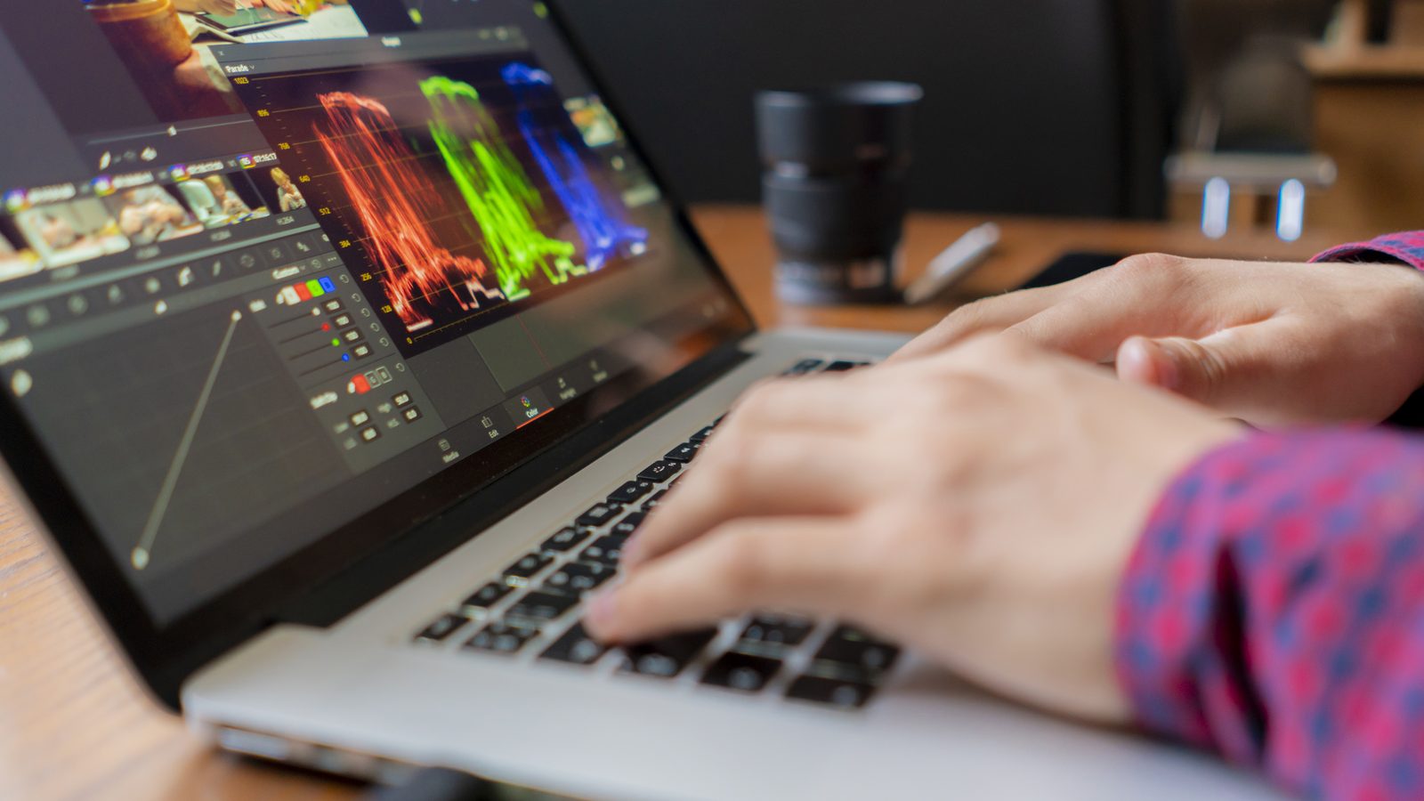 Hands work on a laptop showing a color grading program with bright color graphs.