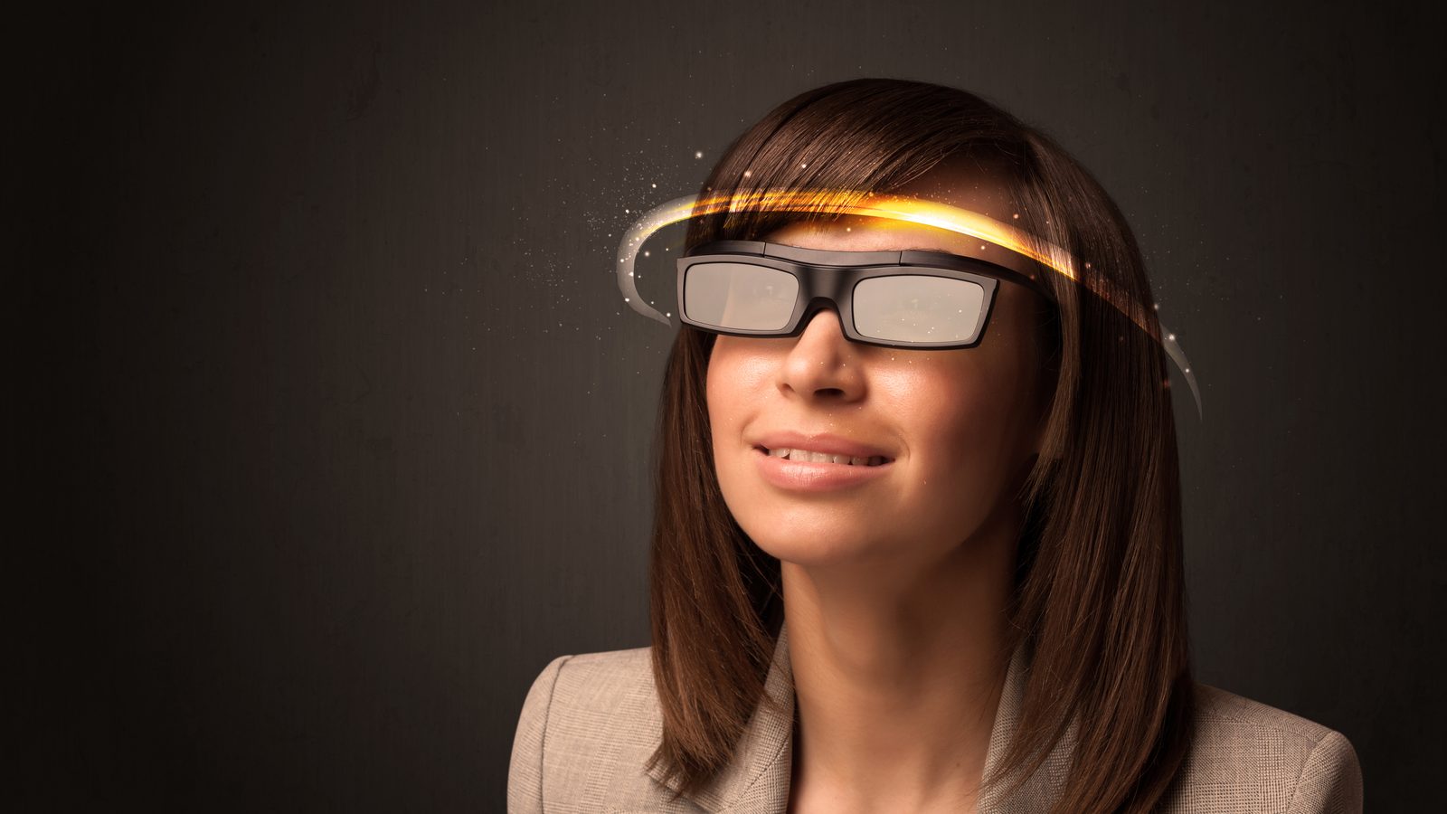A woman in a beige blazer wears chunky smart glasses, with a glowing orange light circling her head.