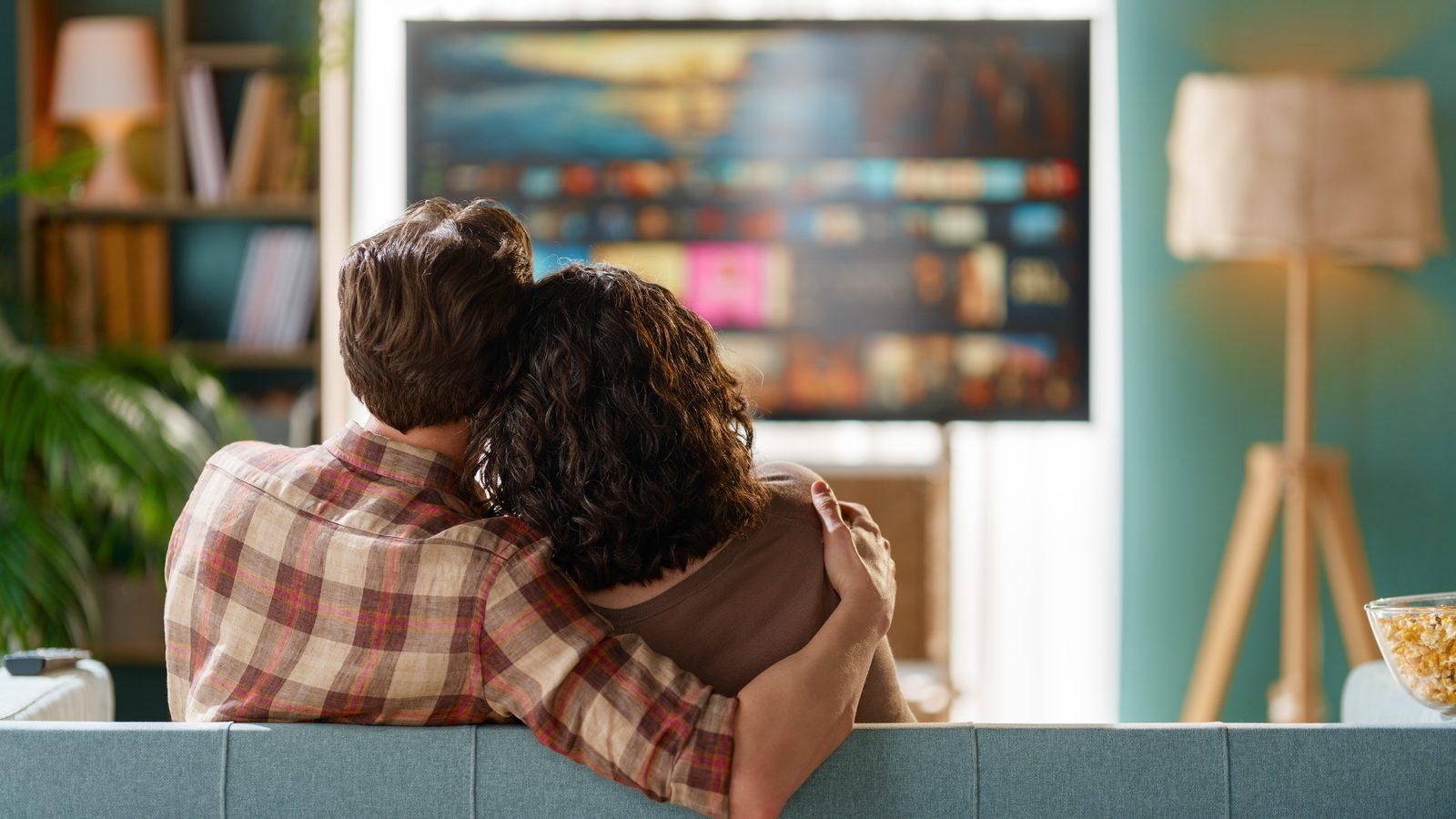 A couple seen from behind on a sofa, watching a TV that shows a blurred grid of colorful video tiles.
